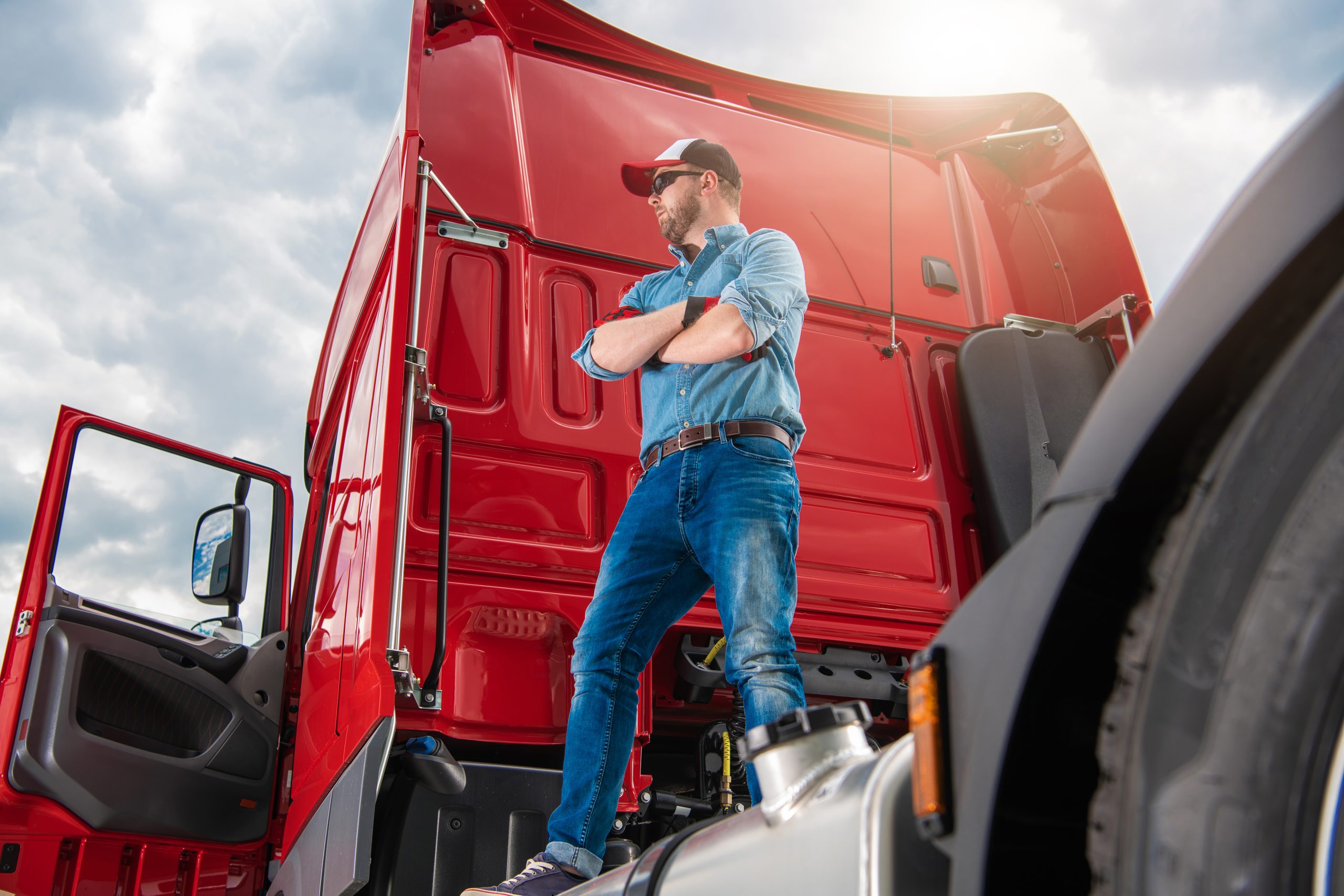 Proud Trucker in His 30s and His Brand New Semi Truck Tractor. Truck Driver Staying on Top of the Vehicle Rear End. Heavy Duty Transportation Industry.